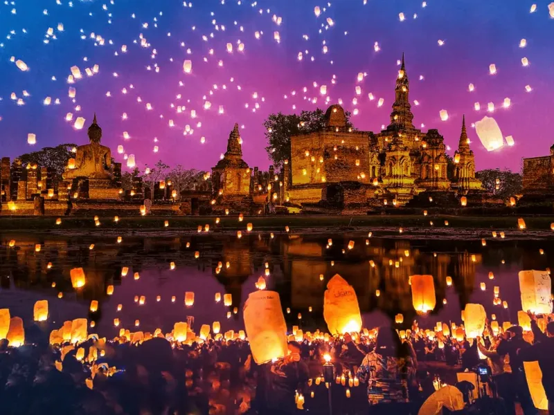 Hình ảnh Lễ hội Loy Krathong ở Thái Lan vào buổi tối, có nhiều đèn lồng thả trên trời và đèn hoa đăng trôi trên sông, không khí huyền ảo.