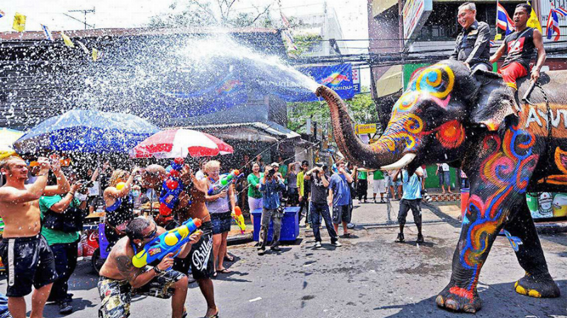 Thời tiết Thái Lan mùa nóng và không khí lễ hội Songkran sôi động với mọi người té nước vui vẻ trên đường phố, du khách tham gia nhiệt tình dưới nắng vàng.